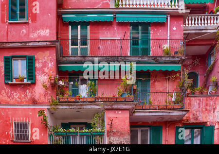 Street view of artistic vibrant pink and green building facade with shuttered windows, balconies, and potted plants. Italy's Amalfi Coast. Stock Photo