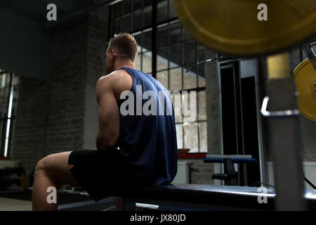 man sitting on weight bench in gym Stock Photo