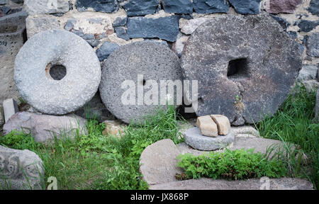 Stone granite wheels with rusted metal rim isolated on green grass near wall Stock Photo