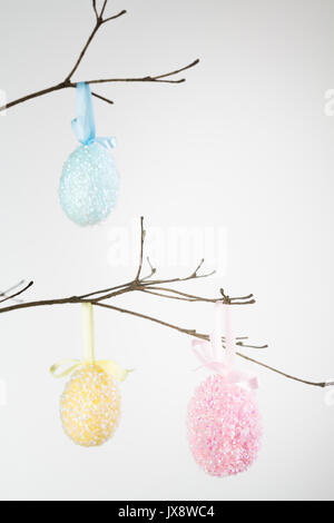 Three sequin encrusted Easter eggs hanging on branch with copy space. Stock Photo