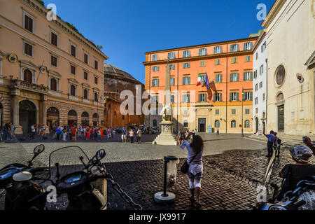 Sunny day in Piazza della Minerva as the back of the Pantheon looms in the background. Tourists and a young lady photograph the elephant obelisk Stock Photo