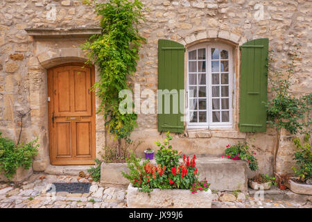 Street view of quaint old stone house facade with a wooden door, shuttered french window, and colorful potted plants. Provence, France. Stock Photo