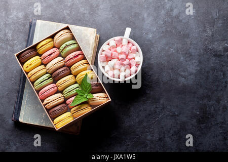 Colorful macaroons in a gift box and marshmallow in coffee cup on stone table. Sweet macarons. Top view with copy space Stock Photo