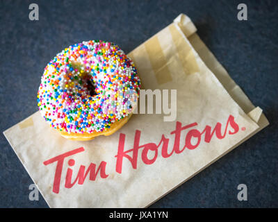A vanilla dip donut (sprinkle donut, rainbow sprinkle donut) from Tim Hortons, a popular Canadian fast food restaurant and donut shop. Stock Photo
