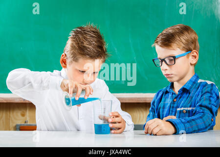 Two small schoolmates pouring blue liquid in glass on lesson in school Stock Photo