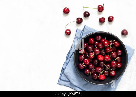 Sweet cherries in black bowl on bright grey background. Flat lay top view Stock Photo
