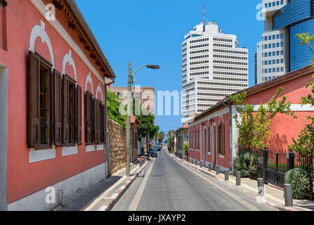 Colorful houses along narrow street as modern buildings on background under blue sky in Neve Tzedek neighborhood in Tel Aviv, Israel. Stock Photo