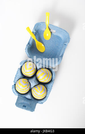Foil covered chocolate easter eggs with plastic spoons in paper box on white background. Stock Photo