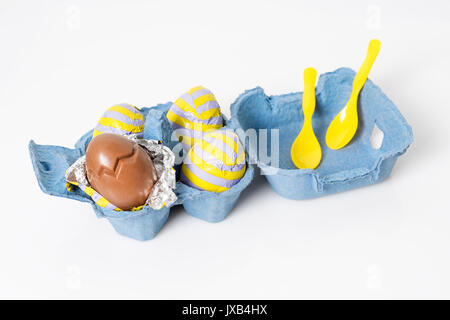Foil covered chocolate easter eggs with plastic spoons in paper box on white background. Stock Photo