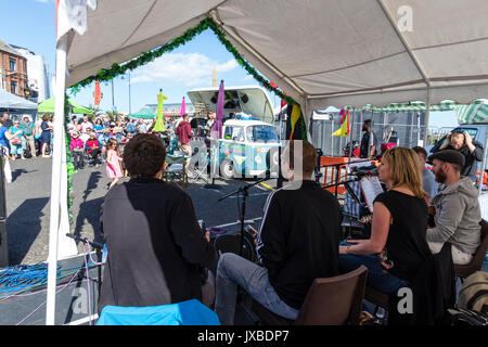 Five person music group Samba Azul sitting on small stage performing during the Ramsgate Festival. View from behind band of small audience. Stock Photo