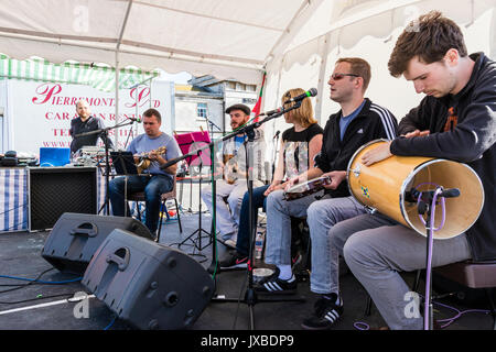 Five person music group Samba Azul sitting on small stage performing during the Ramsgate Festival. Guitarist, singer, drummer and tambourine player. Stock Photo