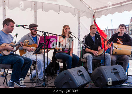 Five person music group Samba Azul sitting on small stage performing during the Ramsgate Festival. Guitarist, singer, drummer and tambourine player. Stock Photo