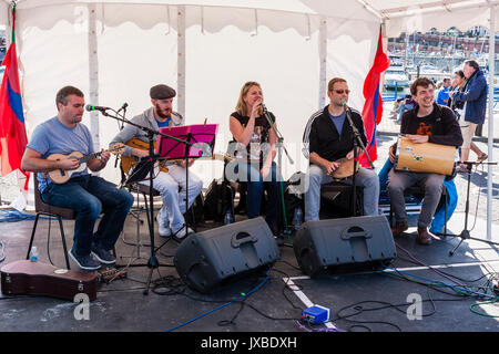 Five person music group Samba Azul sitting on small stage performing during the Ramsgate Festival. Guitarist, singer, drummer and tambourine player. Stock Photo