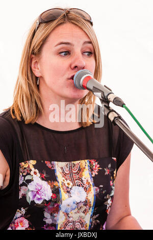 Young Caucasian blond woman, 20s, sitting outdoors, singing into microphone, sunglasses on top of head. Member of the Samba Azul music group. Stock Photo