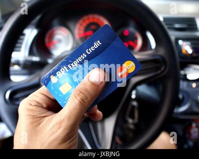 ANGONO, RIZAL, PHILIPPINES - AUGUST 12, 2017: A BPI Expres Credit Mastercard held by a hand in front of a car's steering wheel. Stock Photo