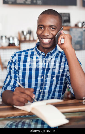 Smiling young entrepreneur talking on a cellphone in his cafe Stock Photo