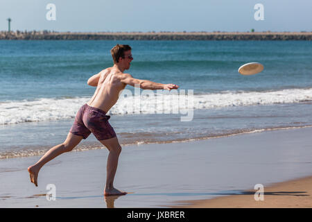 Teenagers boy throwing frisby on beach ocean waterline. Stock Photo