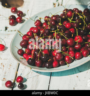 Fresh ripe sweet cherries in plate on rustic light blue wooden garden table, selective focus, square crop. Summer food concept Stock Photo