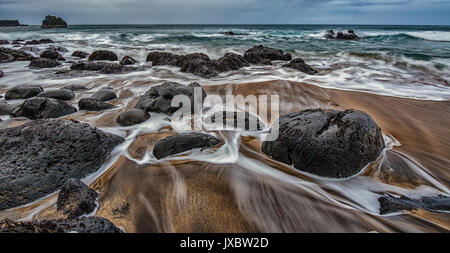 The tide comes in over rocks and sand on the beach at Strondin, Iceland Stock Photo