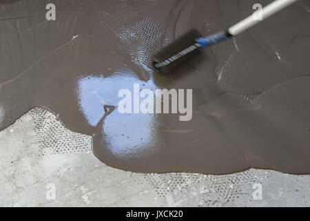 Spreading self leveling plaster with a special roller. Interior of apartment under construction Stock Photo