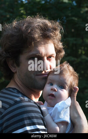 Dad is holding a daughter in his arms for a walk in the park. Spring day, family walk in nature, sunny Stock Photo