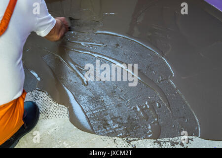 Worker puts a self leveling screed with trowel on cement floor in apartment Stock Photo