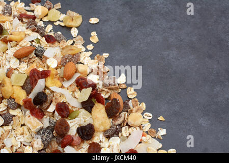 Muesli - cereal flakes with seeds, mixed fruit and nuts - in a diagonal line with copy space on a dark grey slate tile background Stock Photo