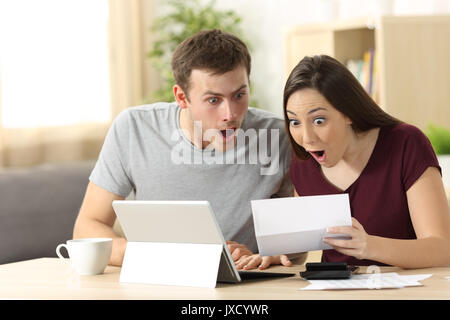 Amazed couple reading together a letter sitting in a desk at home Stock Photo