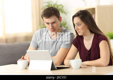 Confused couple receiving on line news sitting in a desk at home Stock Photo