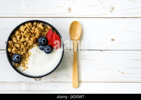 bowl of granola with yogurt, fresh berries, strawberry on wood table. Stock Photo