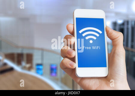 Close-up of hand holding smartphone with free WiFi hotspot icon on the screen to connect to wireless internet, public building interior in background Stock Photo