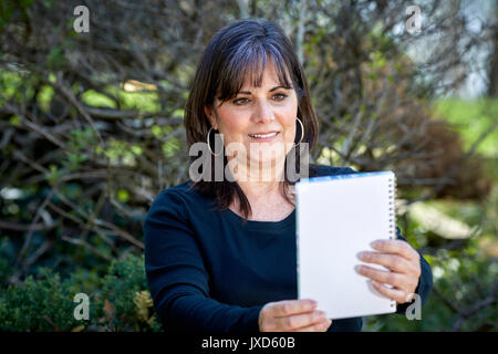 Attractive middle aged woman holding a notebook out so she can read it in an outdoor setting Stock Photo