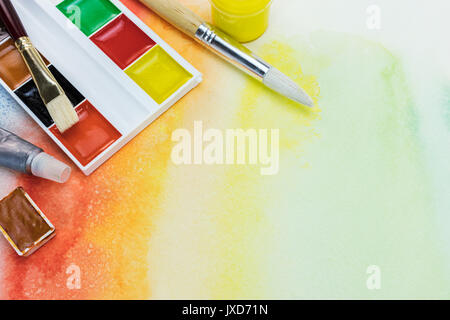 set of watercolor paints and paintbrushes on bright colorful painted background Stock Photo