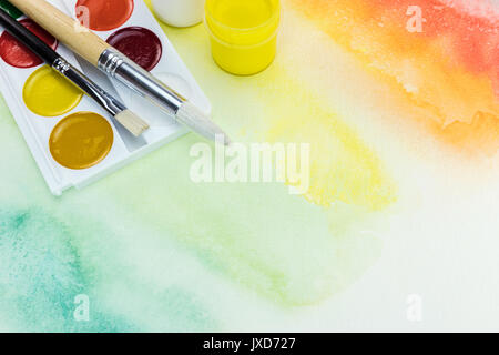 watercolor palette with paintbrushes on multicolored hand painted background Stock Photo
