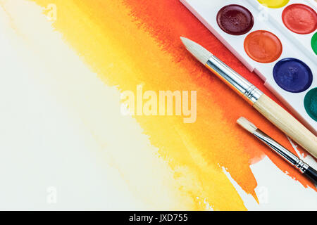 color palette with different brushes on bright red yellow watercolor background Stock Photo