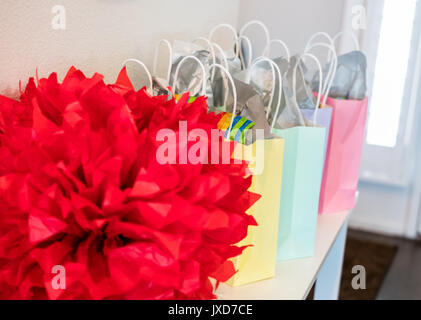 Pastel colored party gift bags with a large red decoration set up on a small table. Stock Photo