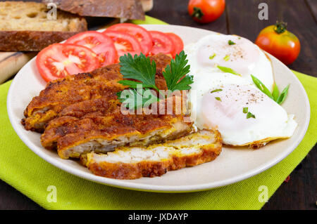 Pieces of chop (schnitzel), toast with eggs, fresh tomato on a dark wooden background. Stock Photo