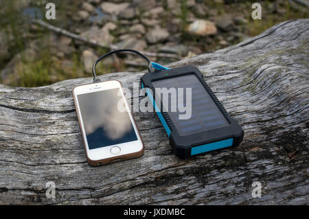 Portable solar panel for charging mobile devices lying on a log in the woods Stock Photo