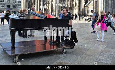 Man playing on grand piano in pedestrian zone in front of Cologne Cathedral main entrance Stock Photo