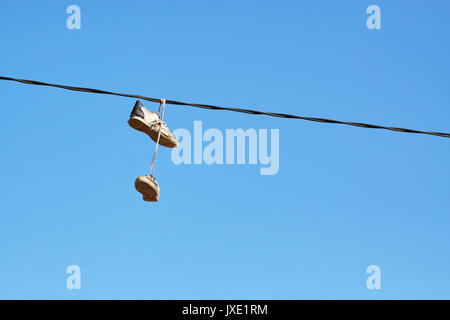 Pair of old shoes hanging on power line against blue sky, space for text. Stock Photo
