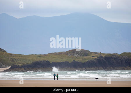 A couple walking their dog along Newborough Beach with Llanddwyn Island or Ynys Llanddwyn behind them and Snowdonia National Park Mountains in the distance, Newborough, Anglesey, Wales, UK Stock Photo