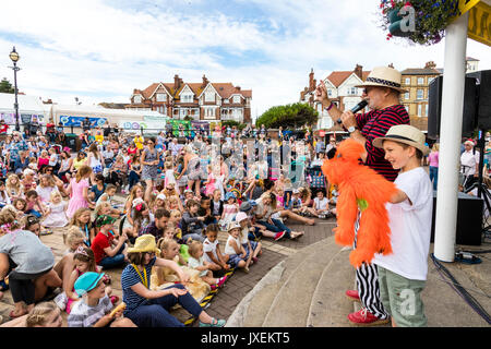 England, Broadstairs folk week. Hobby Horse Club Meeting. Mick Scott on stage hosting the morning's show. Young boy next to him with large orange puppet dog. Stock Photo