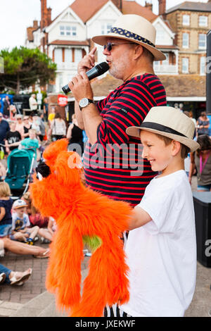 England, Broadstairs folk week. Hobby Horse Club Meeting. Mick Scott on stage hosting the morning's show. Young boy next to him with large orange puppet dog. Stock Photo