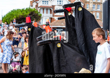 England, Broadstairs folk week. Festival icon, Hooded horses on bandstand looking out at audience during Hobby Horse Club. Wearing red fez hats, young boy standing next to them smiling. Side view. Stock Photo