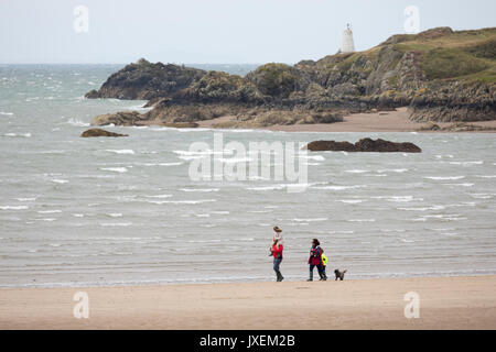 A couple walking their dog along Newborough Beach with Llanddwyn Island or Ynys Llanddwyn behind them and Snowdonia National Park Mountains in the distance, Newborough, Anglesey, Wales, UK Stock Photo