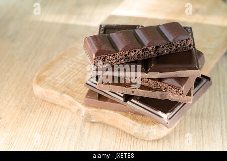 Different broken chocolate bars stacked on a wooden board. Chocolate, lit by the sun. Place for text. Stock Photo