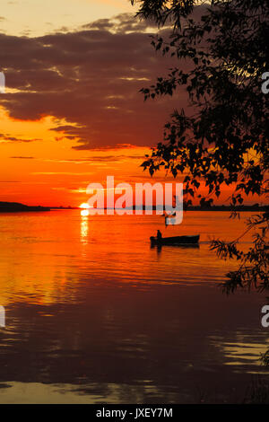 Beautiful sunset at a river with a boat sailing on it. Orange colors reflecting in the water. Stock Photo