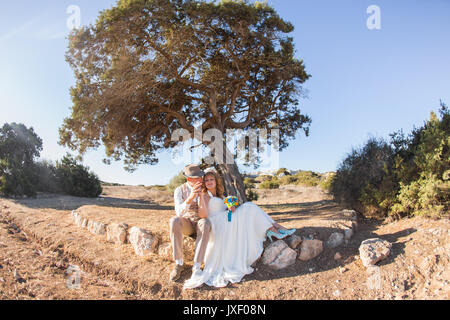 Newlywed couple sitting under shade of tree in summer. Stock Photo