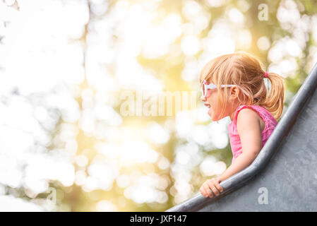 Close-up image with a  little girl having fun on a slide from a playground, on a sunny day.