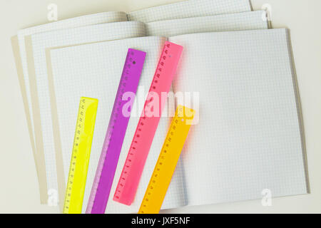 Close-up of a set of colored rulers on a background of large open blank and empty notebooks in a cage, top view, texture. Place for text, the concept of starting school Stock Photo